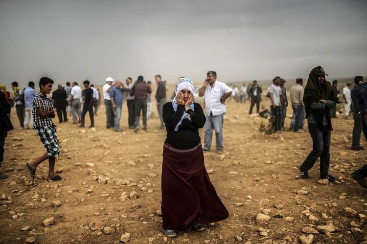 fot. Bulent Kilic / AFP / Getty Images / 24 września 2014
Kobieta przeciera oczy z piasku - zebrani na wzgórzu obserwują starcia pomiędzy ISIS a Kurdami